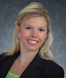 Melody Manning Melody Manning headshot, business woman with blonde hair is wearing a black suit and is pictured in front of a blue gray backdrop