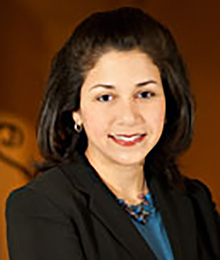 Michelle Bedoya Barnett Michelle Bedoya Barnett headshot, business woman with brown hair wearing a black suit with a blue shirt and necklace, pictured in front of a brown backdrop