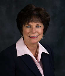 Michelle Jernigan Michelle Jernigan headshot, Caucasian woman with short brown hair, wearing a black suit and pink button down shirt, pictured in front of a dark gray backdrop