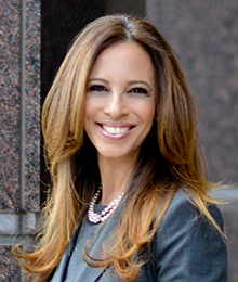 Michelle Suskauer Michelle Suskauer headshot, young businesswoman smiling, she is photographed outdoors in front of a building, wearing a professional gray outfit and pearls