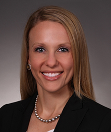 Elisa D'Amico Elisa D'Amico headshot, Caucasian female with blonde hair wearing a black blazer and pearls, pictured in front of a beige backdrop
