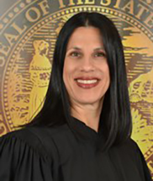 Honorable Laura Anne Stuzin Honorable Laura Anne Stuzin, pictured in front of a large gold seal wearing a standard black academic judge gown