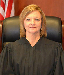 Honorable Margaret Hudson Honorable Margaret Hudson headshot, Caucasian woman with short light brown hair is pictured in a large leather chair with an American flag behind her