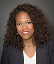 Kamilah Perry Kamilah Perry headshot, African American businesswoman with dark curly hair is wearing a black suit with a white shirt, pictured in front of a gray backdrop