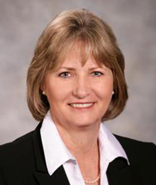 Kelly Sullivan Kelly Sullivan headshot, Caucasian business woman with sandy blonde hair is wearing an black suit with a white button down shirt
