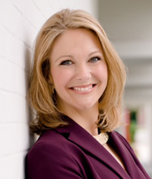 Melanie Griffin Melanie Griffin headshot, professional looking Caucasian woman leaning against a wall, smiling, she has blonde hair and is wearing a plum colored suit