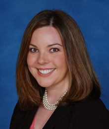 Miller headshot Miller, Caucasian female with brown hair wearing a black blazer and pearl necklace, pictured in front of a blue backdrop